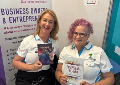Two coaches holding Dr Elana Siew's books Competence Refined and Business in the Blood at Stand C31