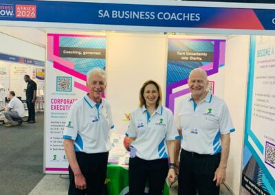 Three SA Business Coaches team members in branded shirts at Stand C31, The Business Show :: Africa 2026